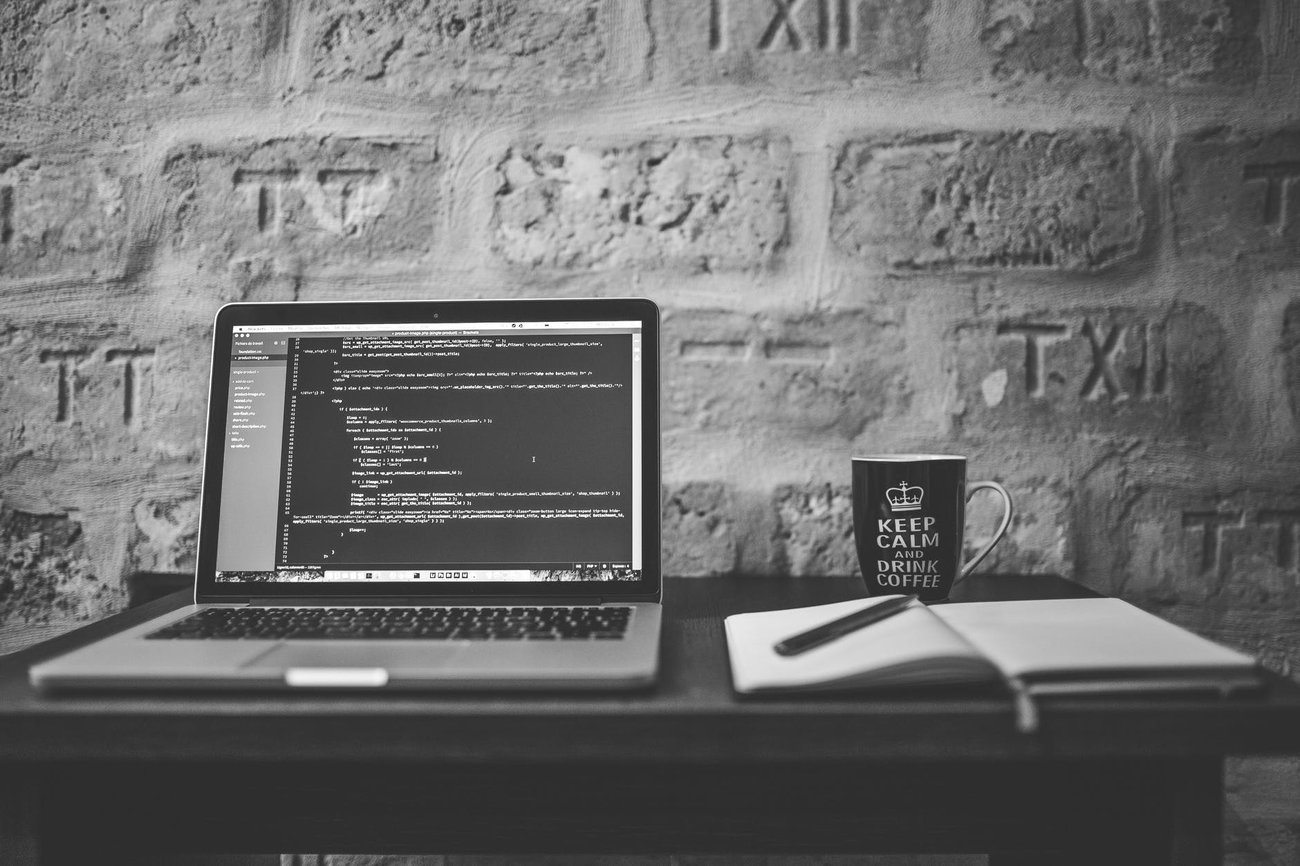 grayscale photo of computer laptop near white notebook and ceramic mug on table