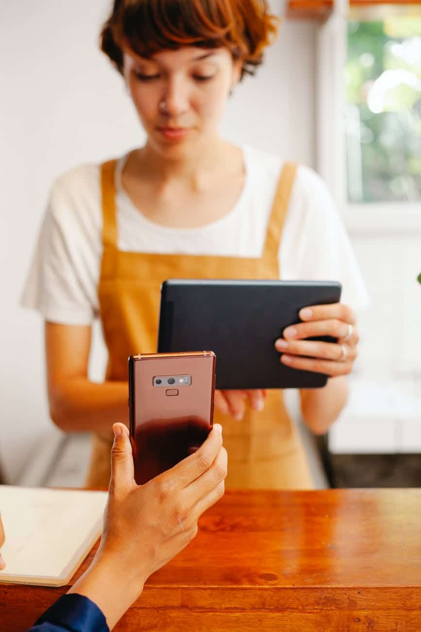 crop worker with tablet against partner with smartphone in cafe